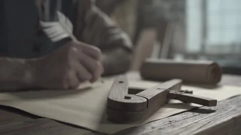 Wooden drafting compass on a table against a blurred medieval inventor writing Stock Footage 337649515