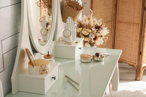 Wooden dressing table with decorative elements and makeup products in room Stock Photos