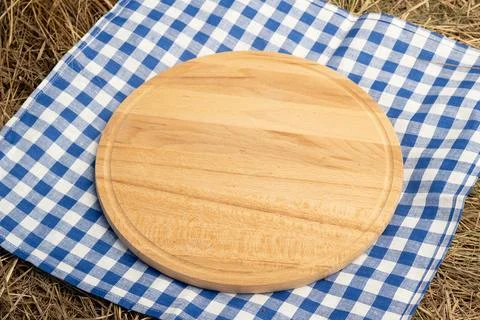 Wooden empty cutting board placed on blue and white checkered picnic blanke.. Stock Photos