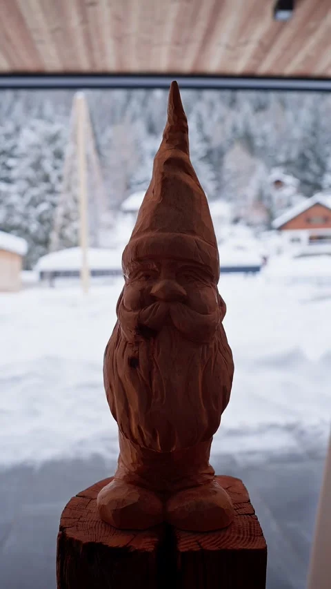 Wooden gnome on split log in alpine chalet with snowy firs beyond Stock Footage 331987712
