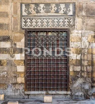 Wooden grunge window with decorated iron grid over stone bricks wall Stock Photos