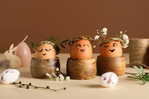 Wooden holders of creative Easter eggs with flowers and leaves on beige table Stock Photos