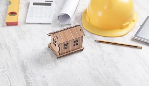 Wooden house model with a helmet, level, document and pencil. Stock Photos