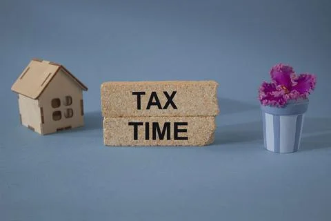 A wooden house sits next to a stack of brick blocks with the word Tax Time. Foto stock