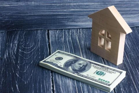 A wooden house stands next to a stack of dolor banknotes. The concept of buyi Stockfoto's