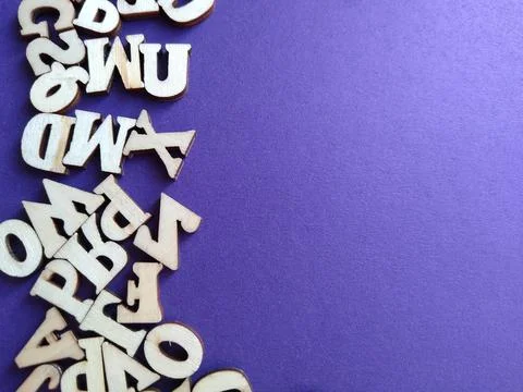 Wooden letters of the alphabet scattered on a purple background with space for Stock Photos
