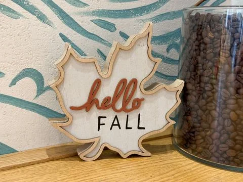 Wooden maple leaf decor with Hello Fall inscription beside coffee beans jar.  Stock Photos