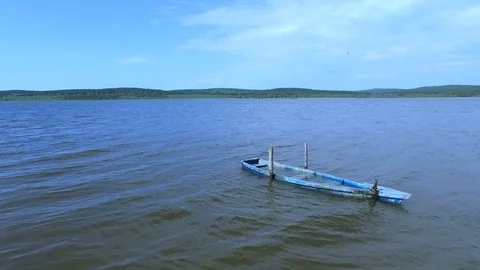 A wooden old boat of blue color on the waves of the lake is filled with water. Stock Footage