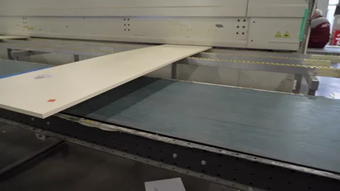 Wooden panel is pulled through a belt sander, and an employee picks up the part Stock Footage 265097499