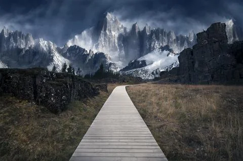 A wooden path through an empty field with massive snowy mountains in the back Stock Photos