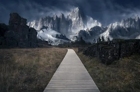 A wooden path through an empty field with massive snowy mountains in the back Stock Photos
