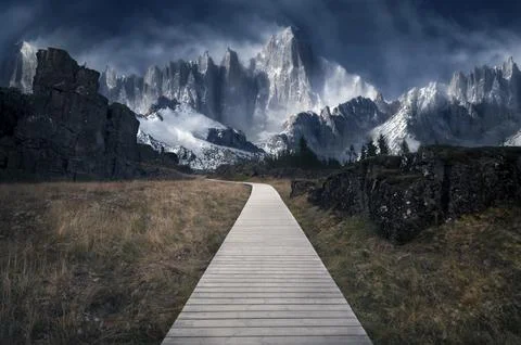 A wooden path through an empty field with massive snowy mountains in the back Stock Photos