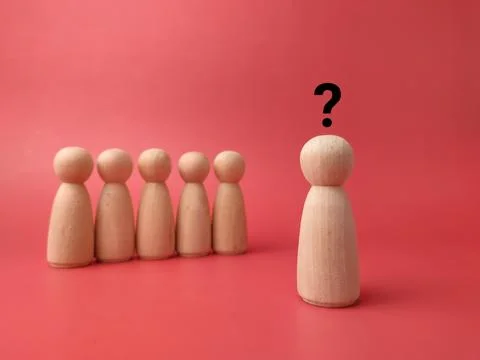A wooden peg figure with a question mark stands apart from five lined-up fi.. Stock Photos
