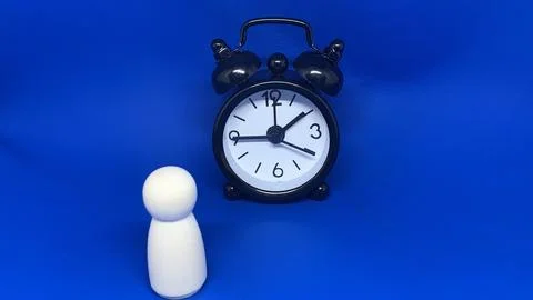 Wooden peg figure standing beside an alarm clock, Stock Photos