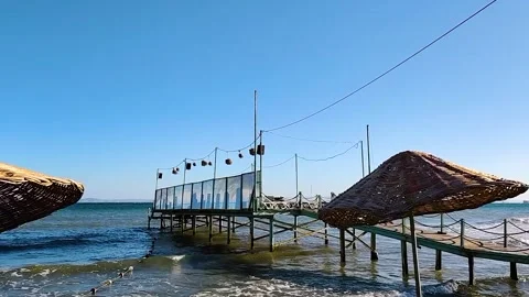 Wooden Pier and Wicker Straw Beach Umbrellas Overlooking Wavy Sea on Summer Stock Footage 344124794