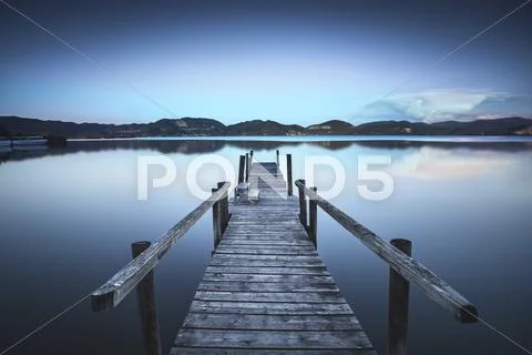 Wooden pier or jetty on blue lake sunset and sky reflection water. Long expos Stock Photos
