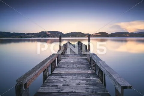 Wooden pier or jetty on blue lake sunset and sky reflection water. Long expos Stock Photos
