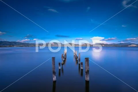 Wooden pier or jetty remains on a blue lake sunset and sky reflection on wate Stock-Fotos