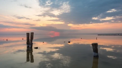 Wooden pillars in front of Sunset clouds reflected in the water of the lake Stock Footage 108208270