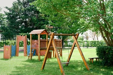 Wooden playground with swings on a green lawn among the trees Stock Photos