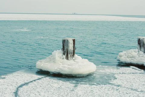 Wooden posts partially covered in ice are surrounded by frozen water on a lak Stock Photos