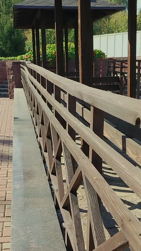 Wooden railing along pathway leading to gazebo in garden with greenery and brick Stock Footage 345858262