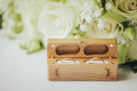 Wooden ring box with two wedding rings placed inside, surrounded by white r.. Stock Photos