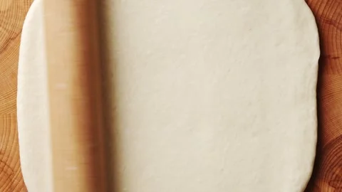 Wooden rolling pin rolls flatbread dough on board. Stock Footage 341429735
