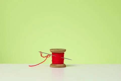 Wooden spool with red wool thread and a large needle on a white table. Handic Stock Photos