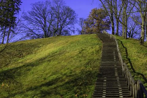 A wooden staircase with leaning weathered steps and a railing rises to the hill Stock Photos