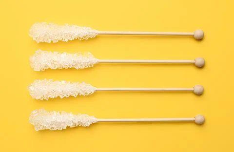 Wooden sticks with sugar crystals on yellow background, flat lay. Tasty rock  Stock Photos