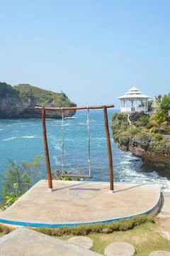 Wooden swing on a cliff overlooking turquoise ocean waves. Stock Photos