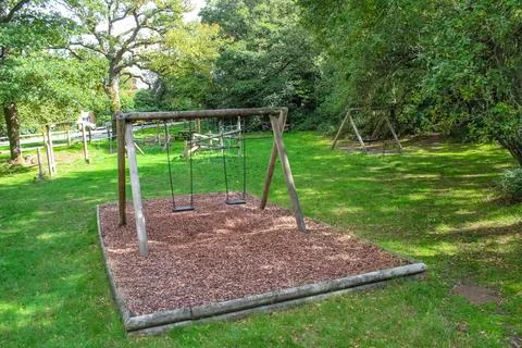 A wooden swing set stands on a rectangular mulch bed in a grassy clearing. Lu Foto stock