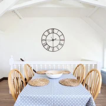Wooden table and chairs with blue spotted cover, attan mats and large clock on Stock Photos