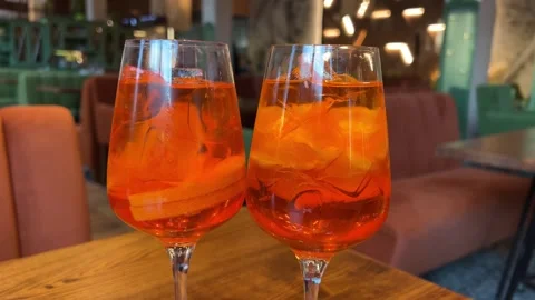 Wooden table desserts Coco and Rose jelly cheesecake and two glasses of Aperol Stock Footage 314097953