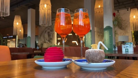 Wooden table desserts Coco and Rose jelly cheesecake and two glasses of Aperol Stock Footage 323920401