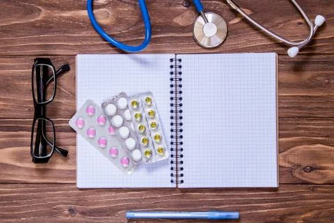 Wooden table with empty note book, pills, glasses, stethoscope Foto stock
