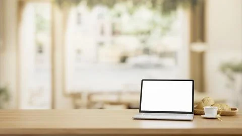 A wooden table features a white-screen laptop computer mockup in a cosy Sca.. イラスト素材