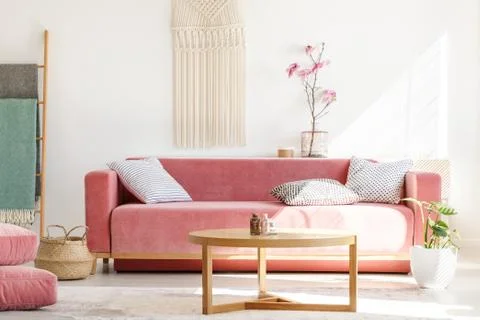 Wooden table in front of red sofa in pastel living room interior with flowers Stock Photos