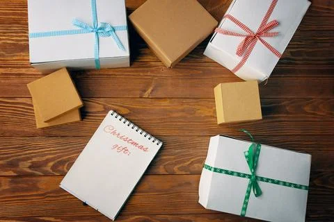 Wooden table with gift boxes and notepad with list of Christmas gifts. Stock Photos