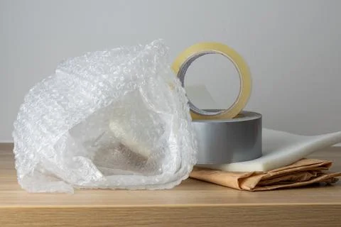 A wooden table holds bubble wrap, tape, and folded paper in a static arrang.. Stock Photos