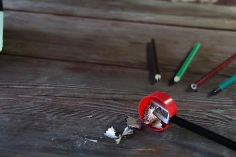 On a wooden table there is a red sharpener and pencil shavings Stock Photos