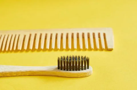 A wooden toothbrush and a wooden comb lie on a yellow background Stock Photos