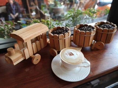 Wooden Train with coffee beans in the buckets and a cup of capucino cofee Stock Photos