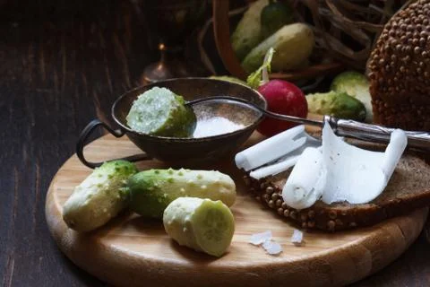 Wooden tray with mini cucumbers, salt shaker and black bread sandwich with lard Stock Photos