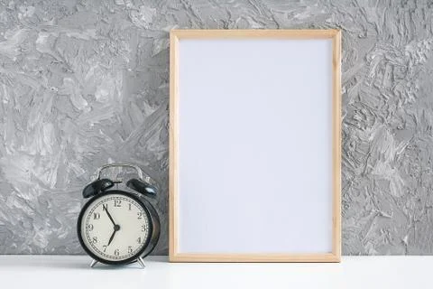 Wooden vertical white empty frame and black alarm clock on table on gray conc Stock Photos