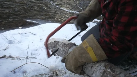 Woods man cutting log using hand saw in winter beside a stream Stock Footage 121220379