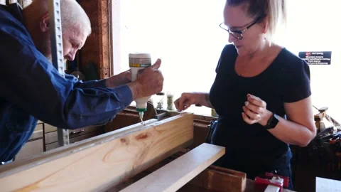 Woodwork biscuit joining glue up timber older gentleman training lady assist Stock Footage 231789558