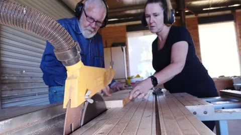Woodwork table saw timber older gentleman training lady assistant first cut Vidéo 231788563