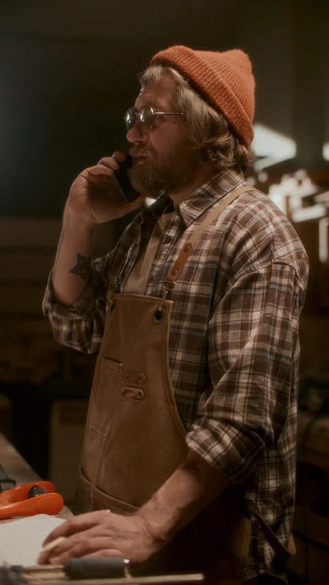 Woodworker Examining Paper Plan and Speaking on Phone in Workshop Video stock 331984696
